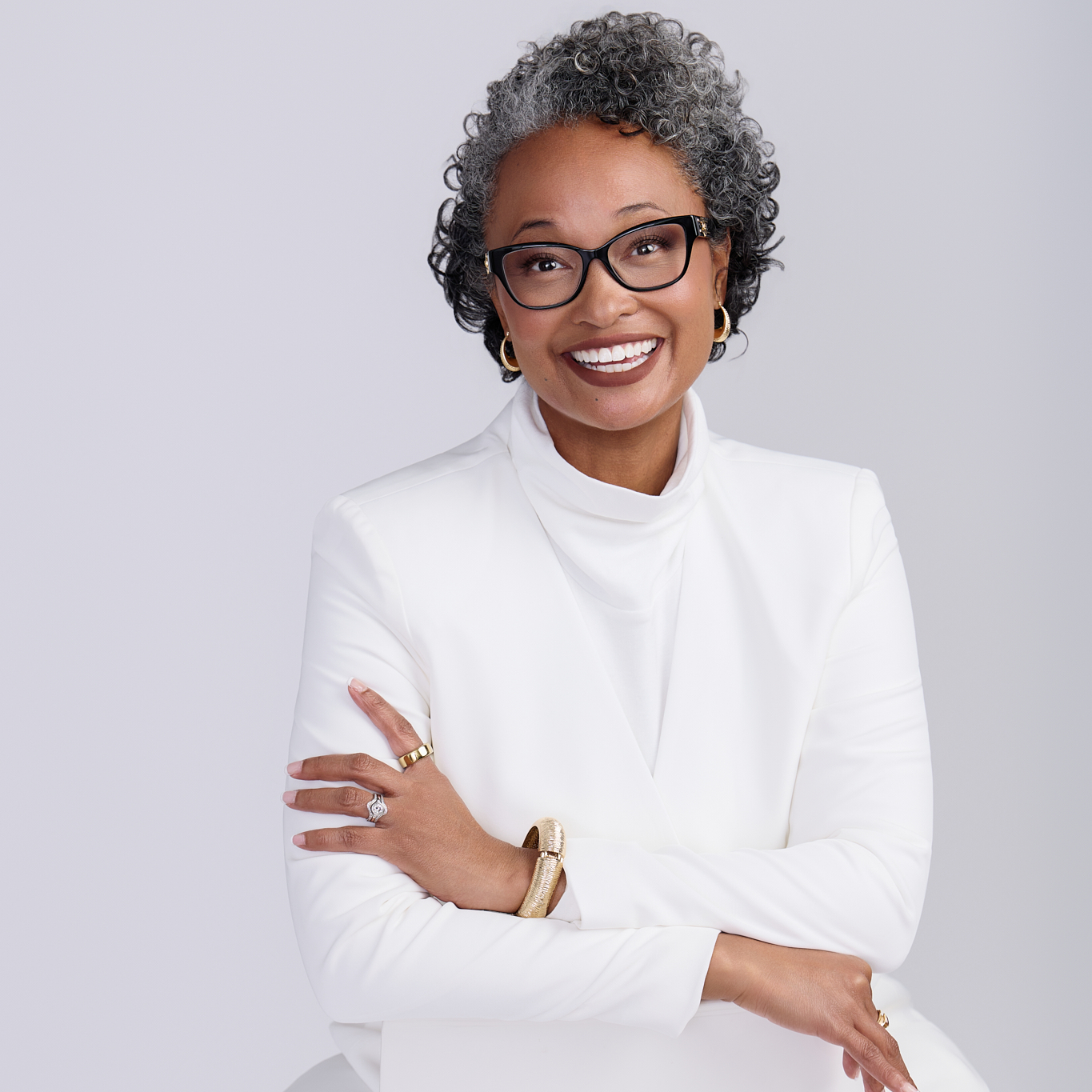 Woman wearing glasses and a white outfit with a plain background